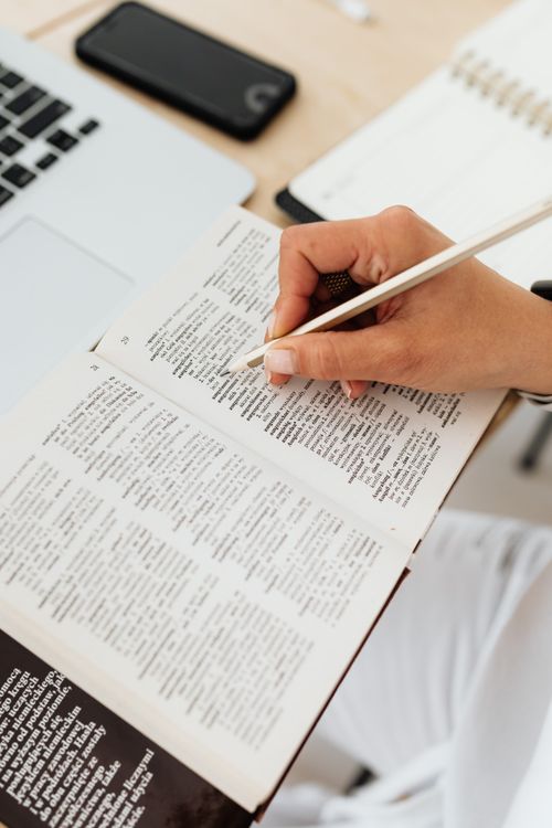 Person practicing word games on a tablet with a notebook of learned words beside them